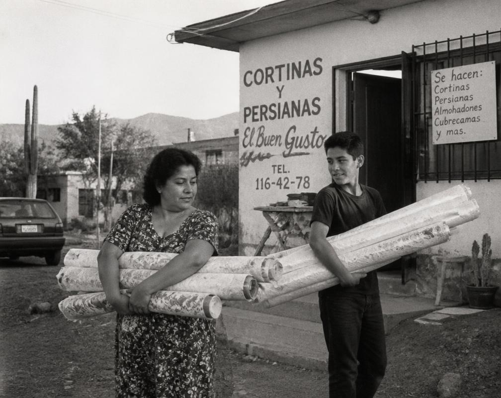 Vintage photograph of the family carrying rolled fabric curtains outside their workshop